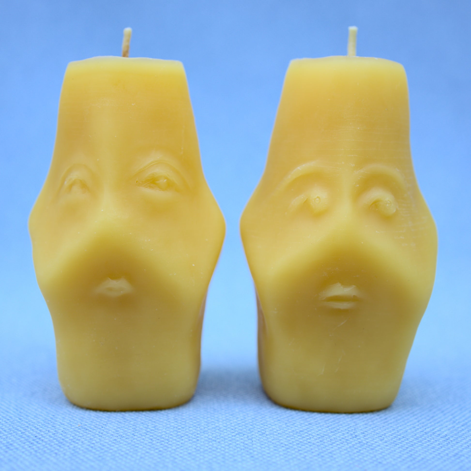 both sides of two faced beeswax candles showing two different hand sculpted faces