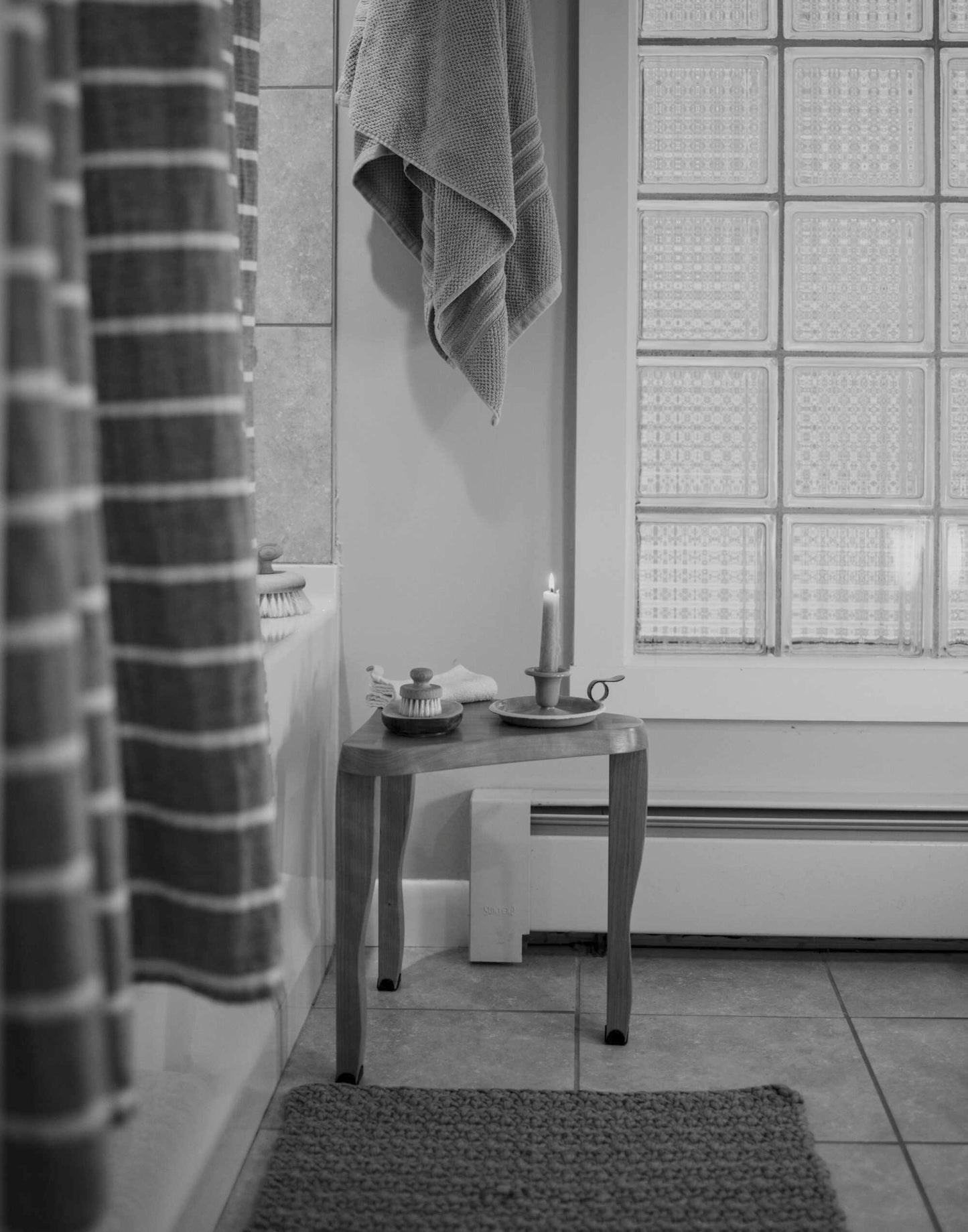 made cozy milking stool dovetailed triangular side table nex to bathtub in bathroom holding candle