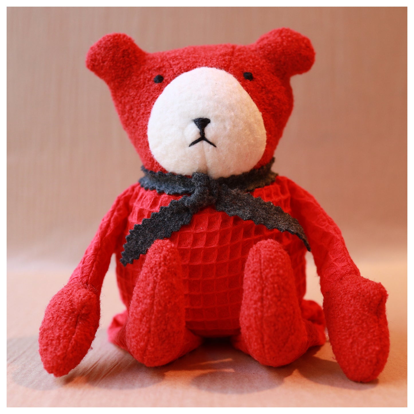 red teddy bear with grey scarf sitting down
