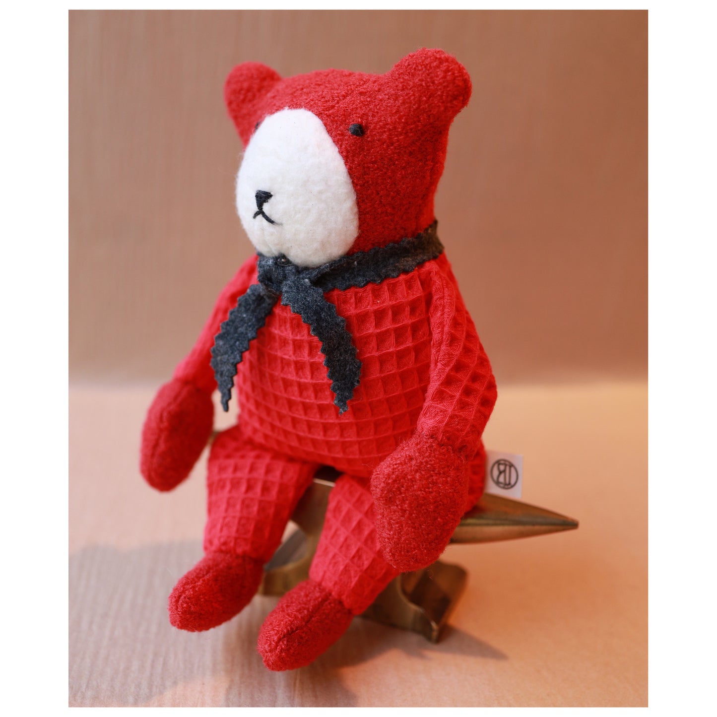 berry sitting on a brass anvil to show posing. Berry is all red with white nose and grey scarf