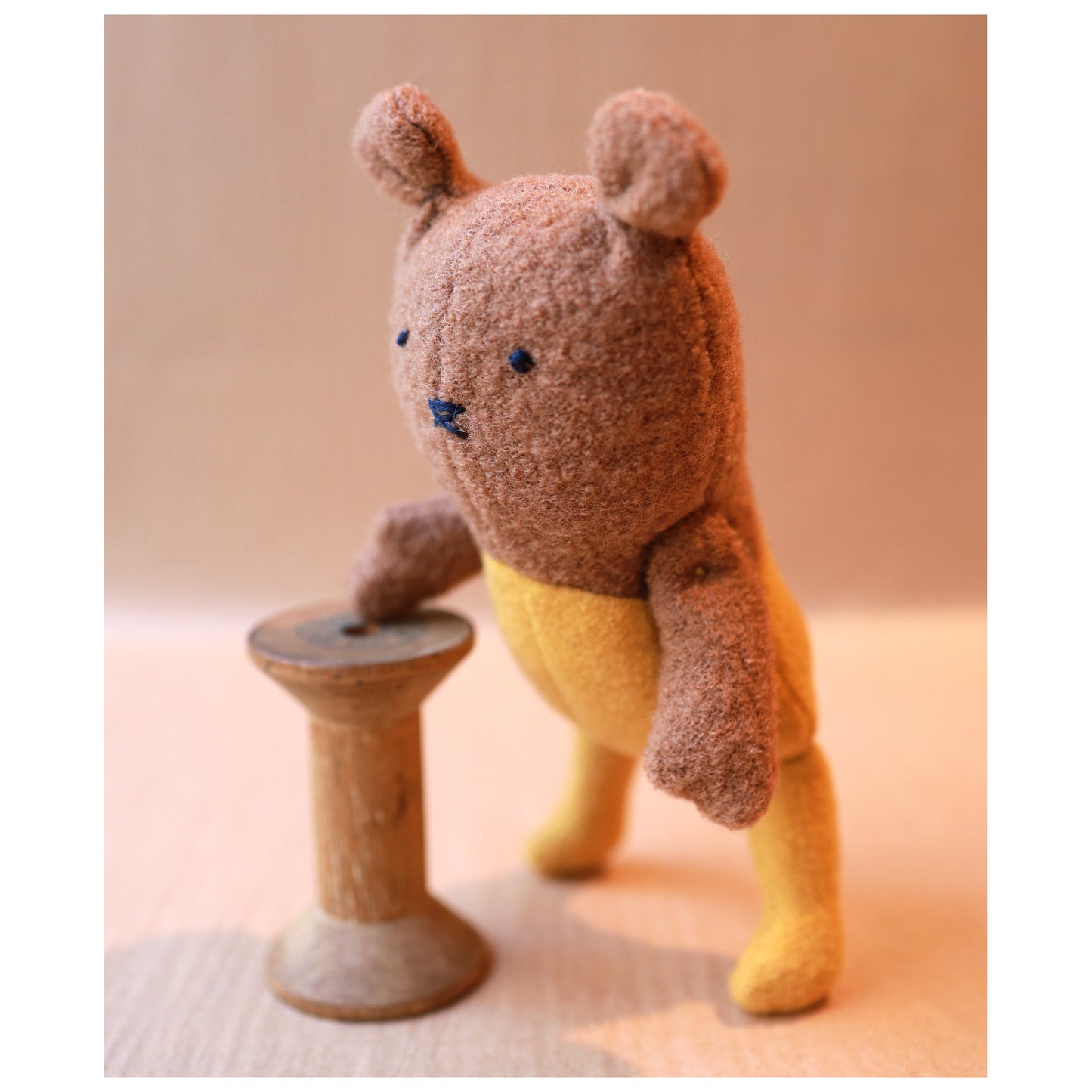 Small brown mouse toy standing on a wooden spool against a beige background