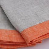 Close up of cloudy gray and mandarin orange bordered linen napkins. Picture frame mitered corner boarder.