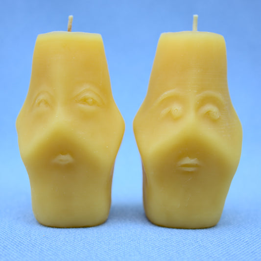 both sides of two faced beeswax candles showing two different hand sculpted faces 