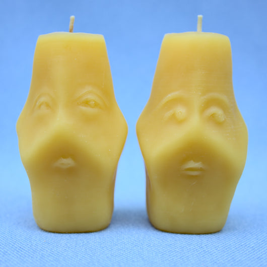 both sides of two faced beeswax candles showing two different hand sculpted faces 