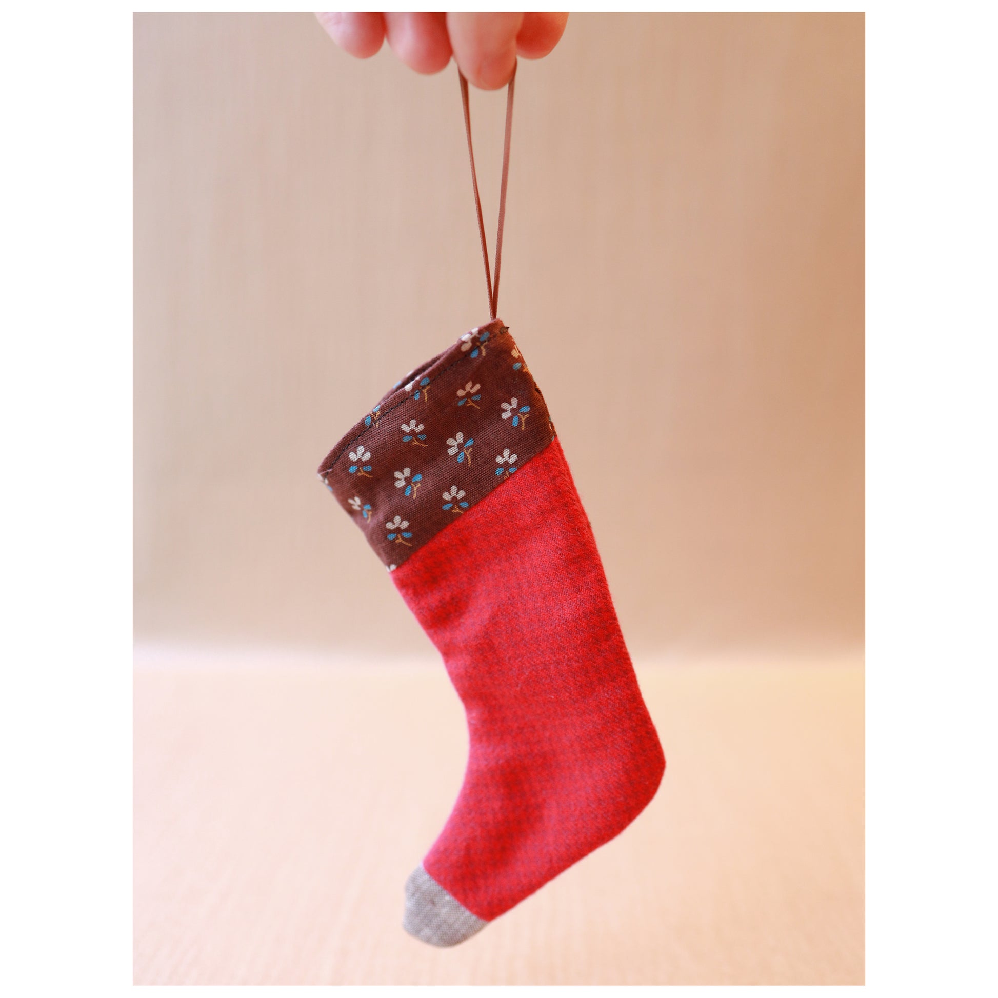 Red Christmas stocking with a brown top held by a hand against a beige background