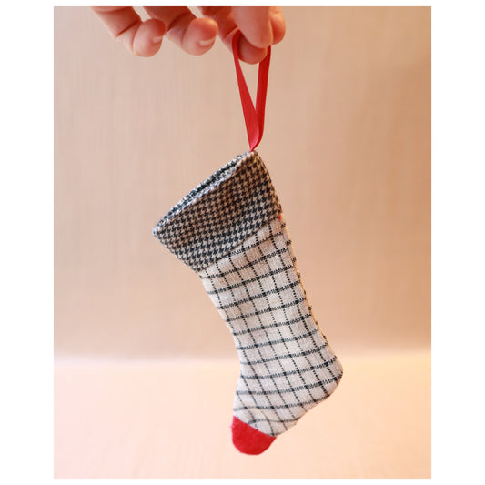 Small checkered stocking with red accents held by a hand against a plain background