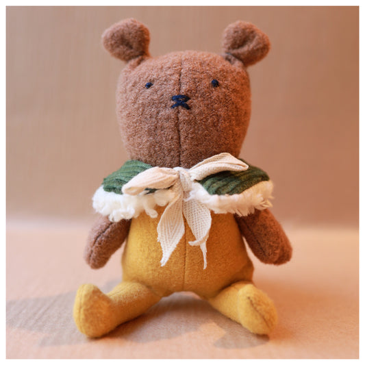 Brown and yellow stuffed animal toy mouse with a green collar and white bow on a beige background