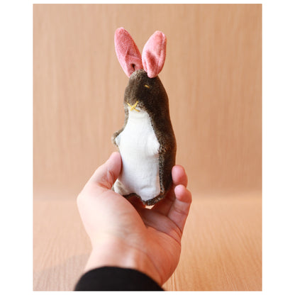 hand holding a small mohair bunny toy with brown mohair, pink ears, and a light blue linen belly