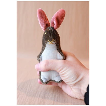 Hand holding a small rabbit-shaped plush toy with pink ears against a beige background
