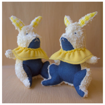 Two plush toys resembling bunnies in blue and yellow outfits on a beige background