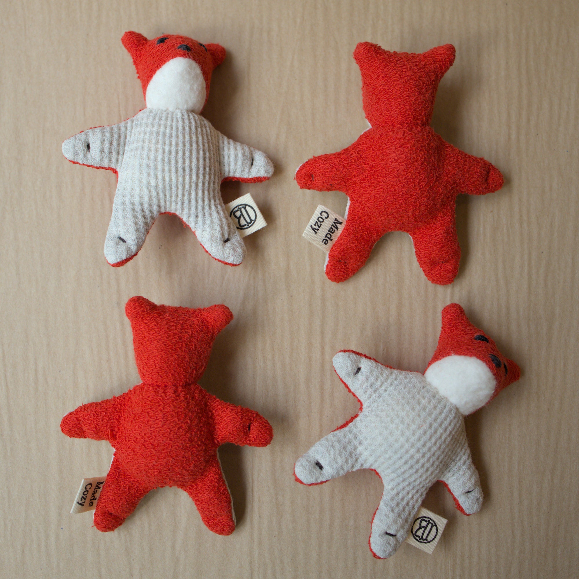 Four red and white stuffed toys resembling foxes on a beige surface.