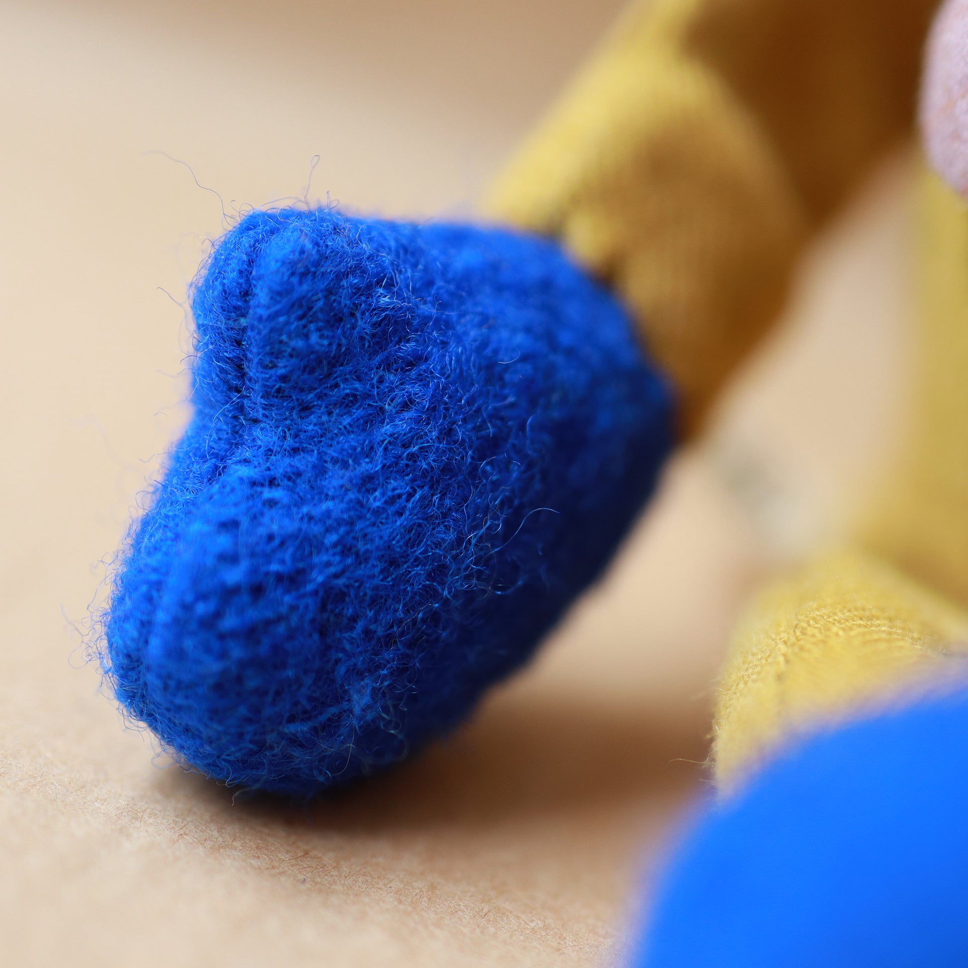 Close-up of a fuzzy blue plush toy foot or paw attached to a yellow plush body, resting on a beige surface.