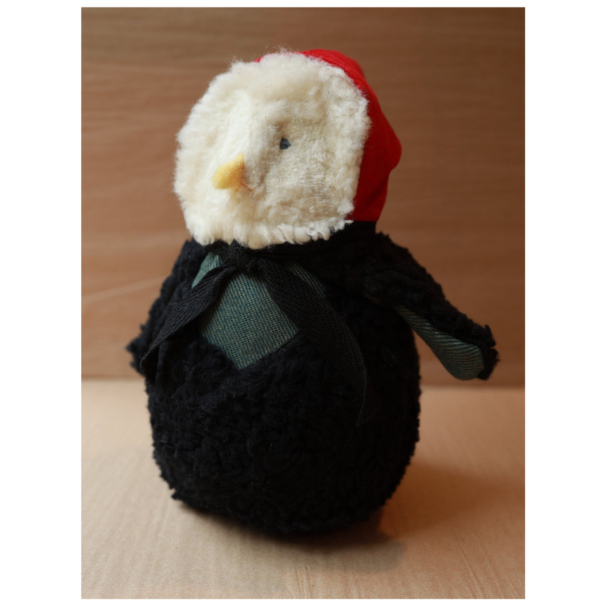 a plush toy owl with a white fluffy face and black body wearing a red hood and a green chest. The beak is yellow felt