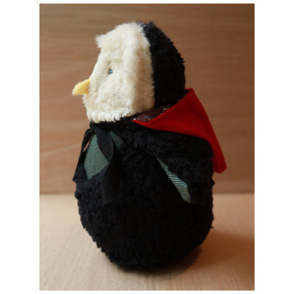 a plush toy owl with a white fluffy face and black body wearing a red hood and a green chest. The beak is yellow felt with the hood down