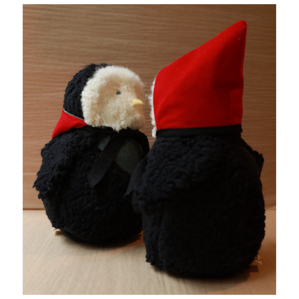 two plush toy owls with a white fluffy face and black body wearing a red hood and a green chest. The beak is yellow felt