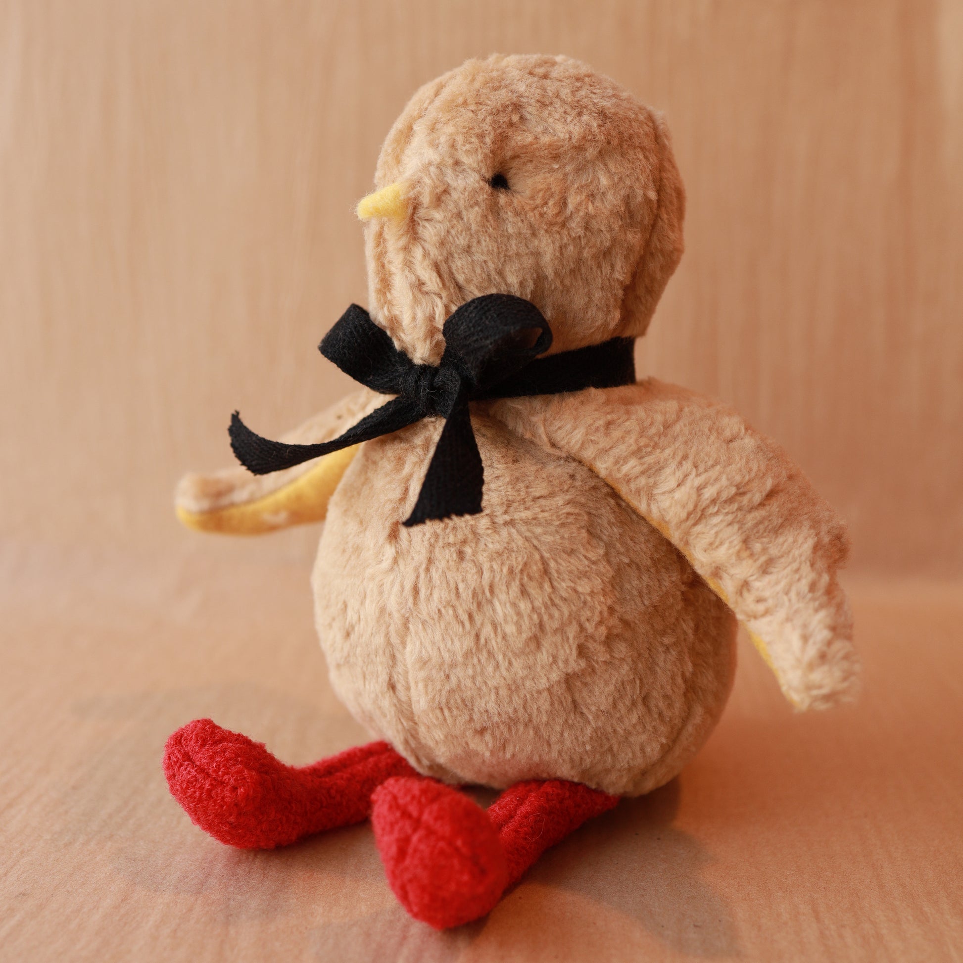 stuffed toy chick with black ribbon and red legs. Brown cotton fur and yellow beak