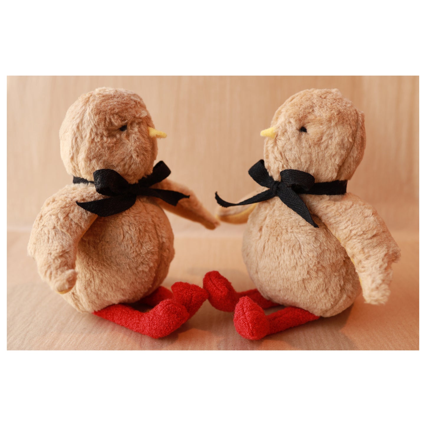 Two plush birds with black ribbons and red legs on a beige background