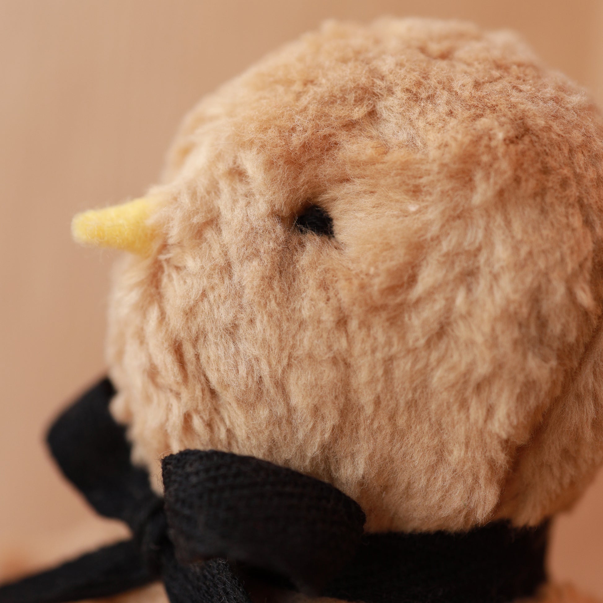 Close-up of a plush toy with a beige face and black accents on a beige background