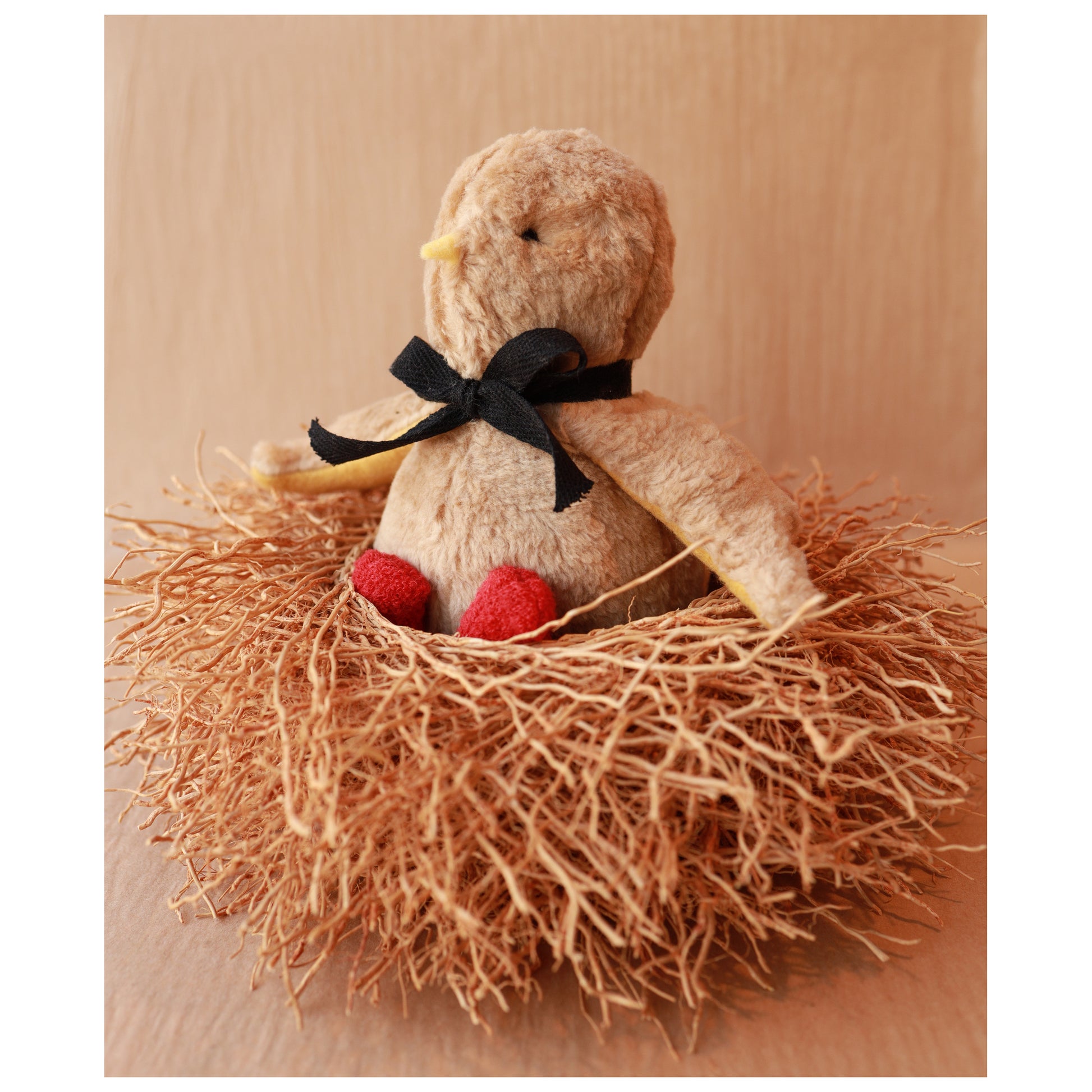 Stuffed bird toy with a black bow in a nest on a brown surface