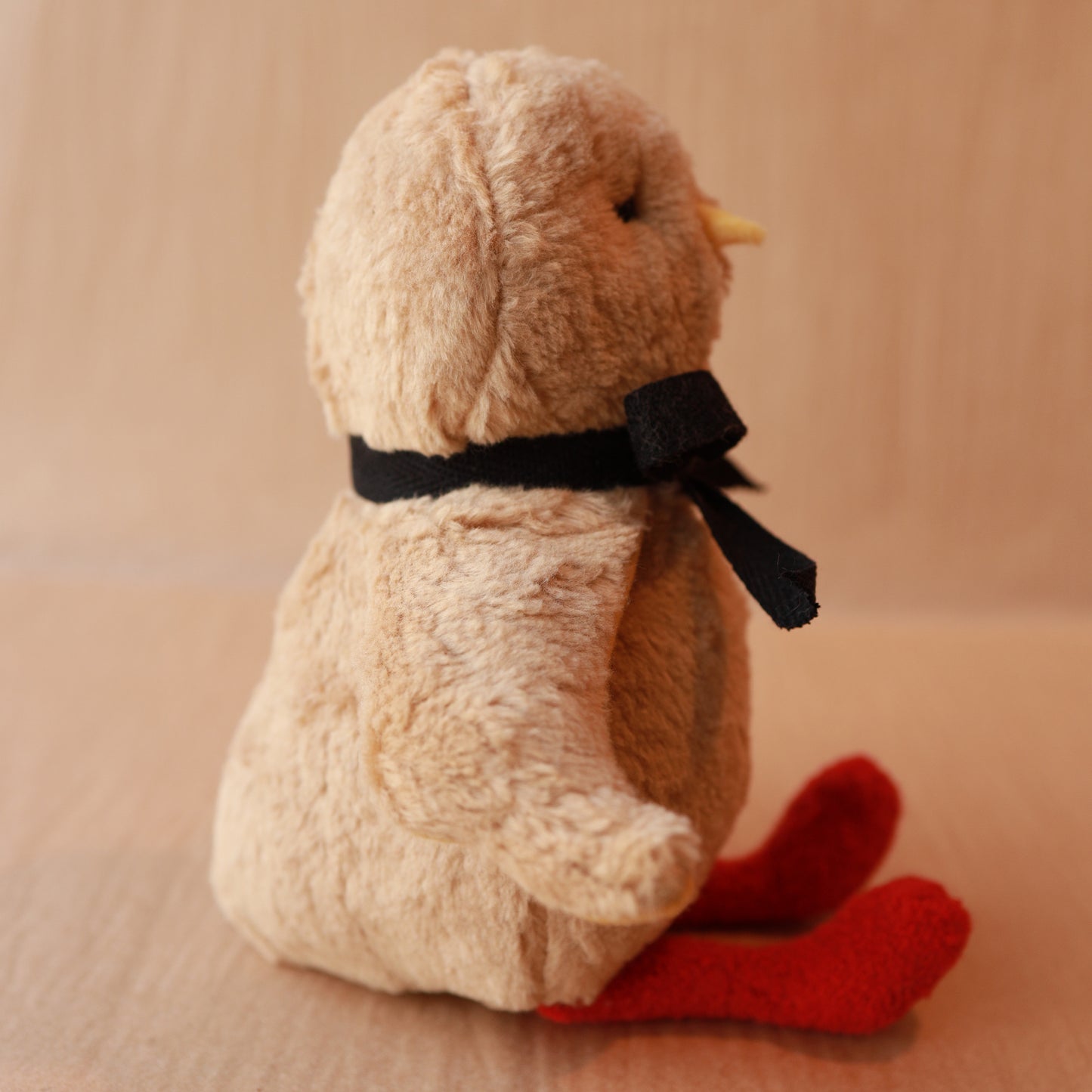 Plush toy chick with a black bow and red feet on a beige background