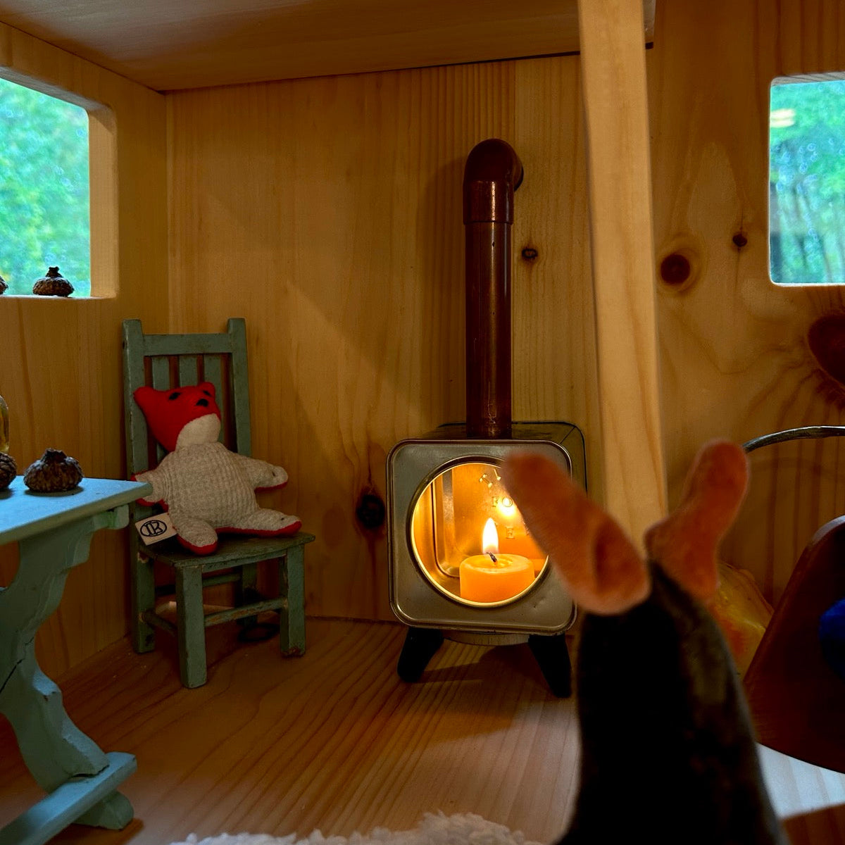 a miniature pine cabin with a woodstove made out of a tea tin and lit with a tealight. Toys gather around it