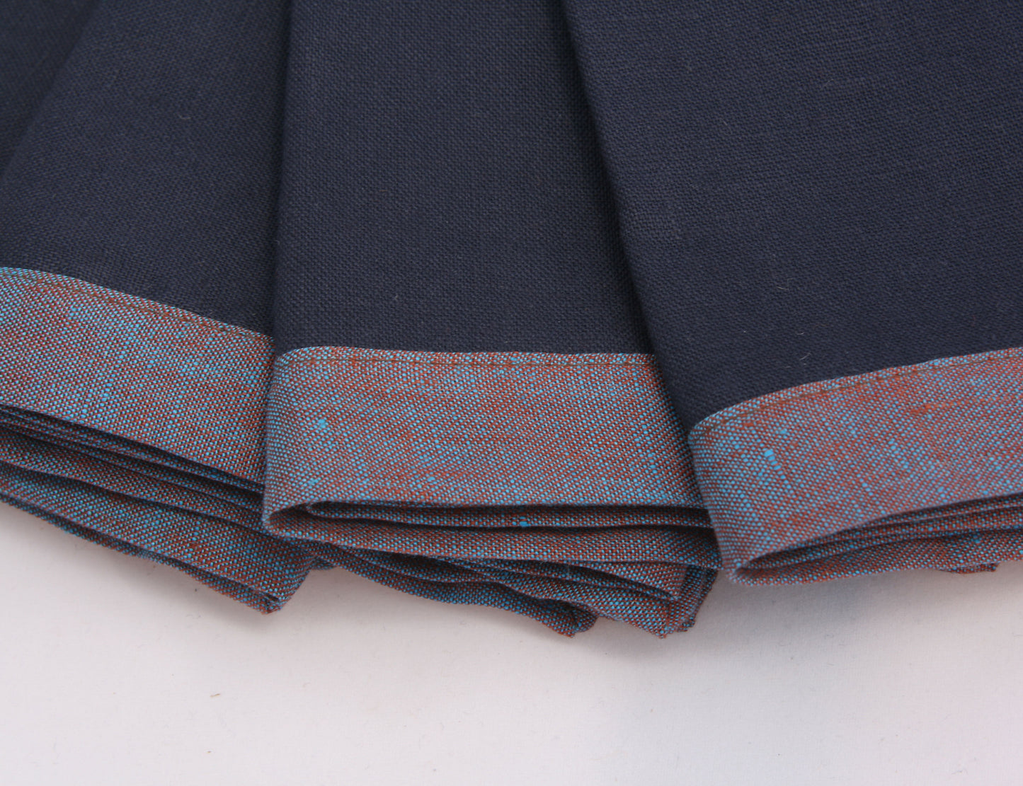 Close up of blueberry blue and reddish blue bordered linen napkins. Picture frame mitered corner boarder.