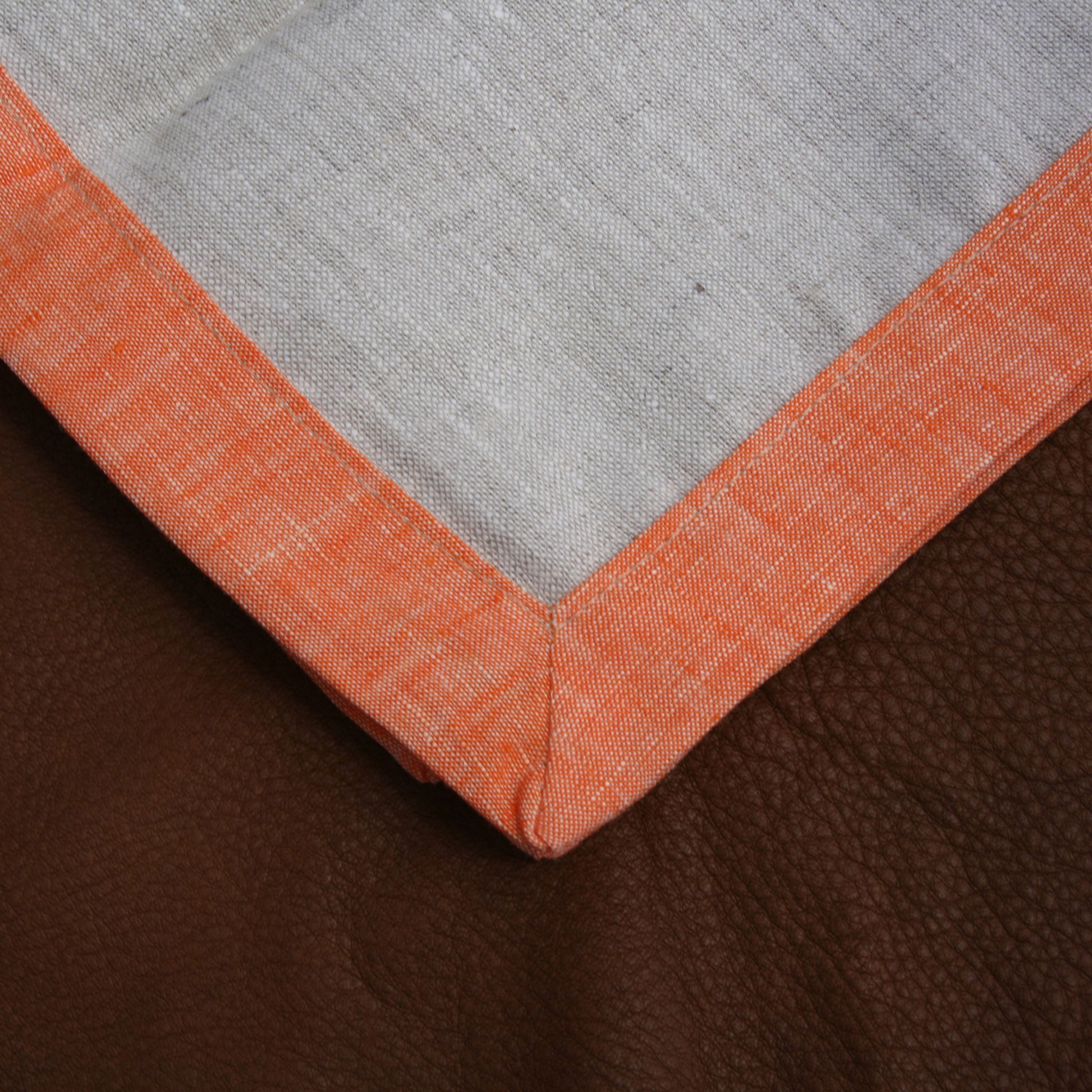 Close up of corner on cloudy gray and mandarin orange bordered linen napkins. Picture frame mitered corner boarder.