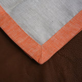 Close up of corner on cloudy gray and mandarin orange bordered linen napkins. Picture frame mitered corner boarder.